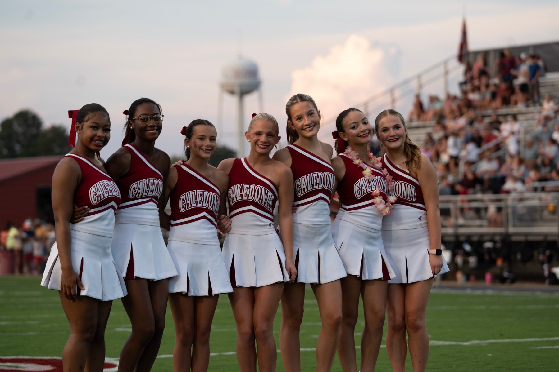 Caledonia's cheerleaders pose arm in arm, the town's water tower and a full home crowd behind them