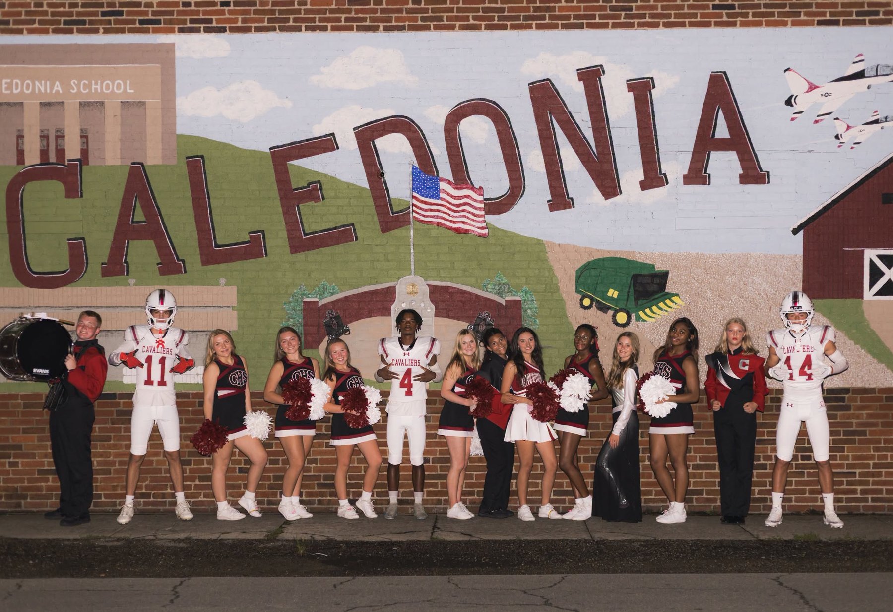 Caledonia's players, cheerleaders and band line up in front of the Caledonia mural