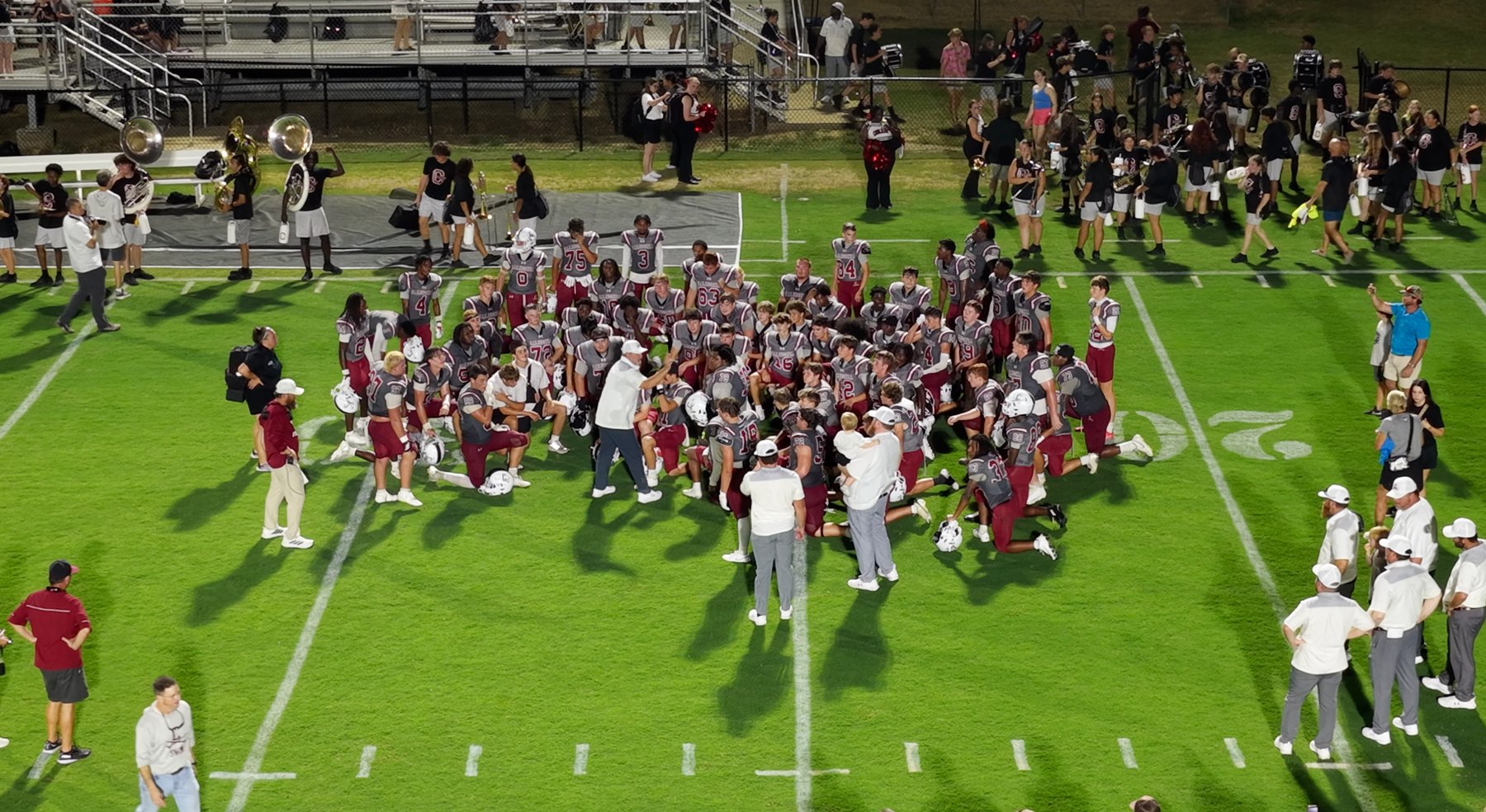 The team kneels together around its coaches on the field after the game, seen from above