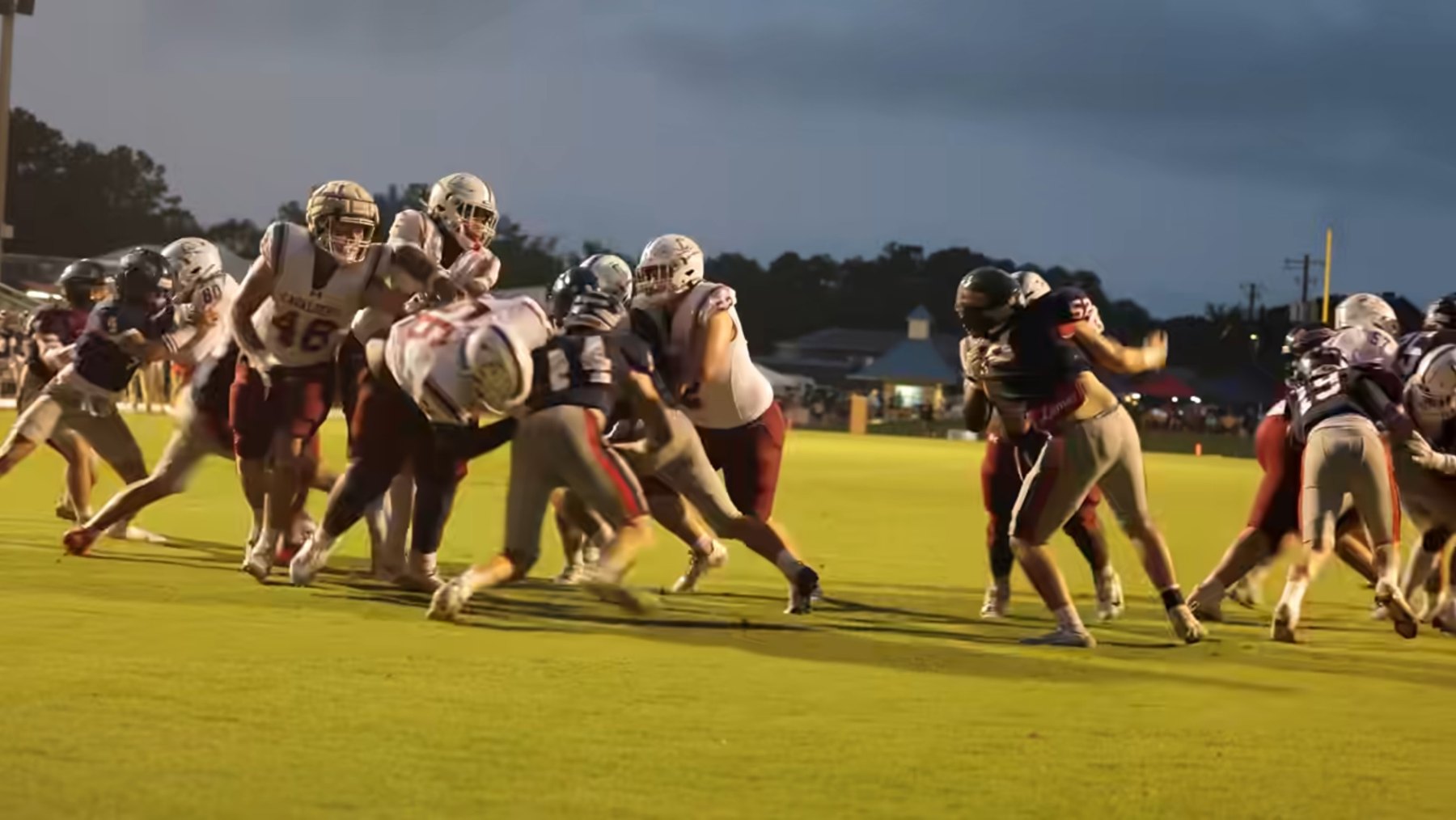 Caledonia's linemen drive into Lamar's defenders under a stormy evening sky